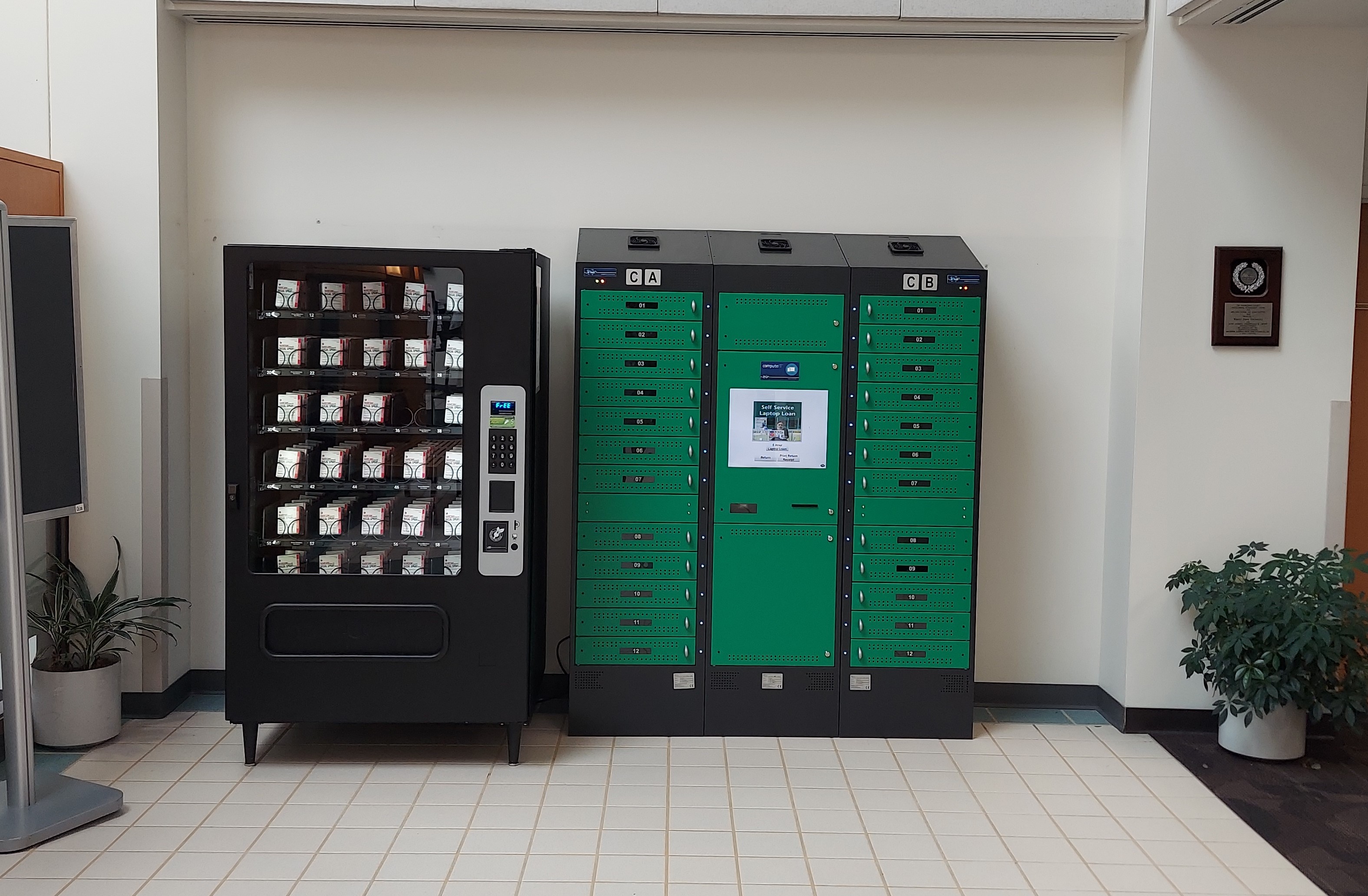 image of a Narcan (naloxone) vending machine on the left wall of the undergraduate library lobby. It stands to the left of a self service laptop machine.